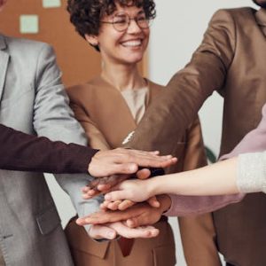 A group of happy, diverse colleagues celebrating teamwork and cooperation with a group high five indoors.