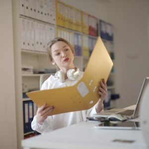 A young woman analyzing documents with concentration in a modern office setting, surrounded by folders and technology.